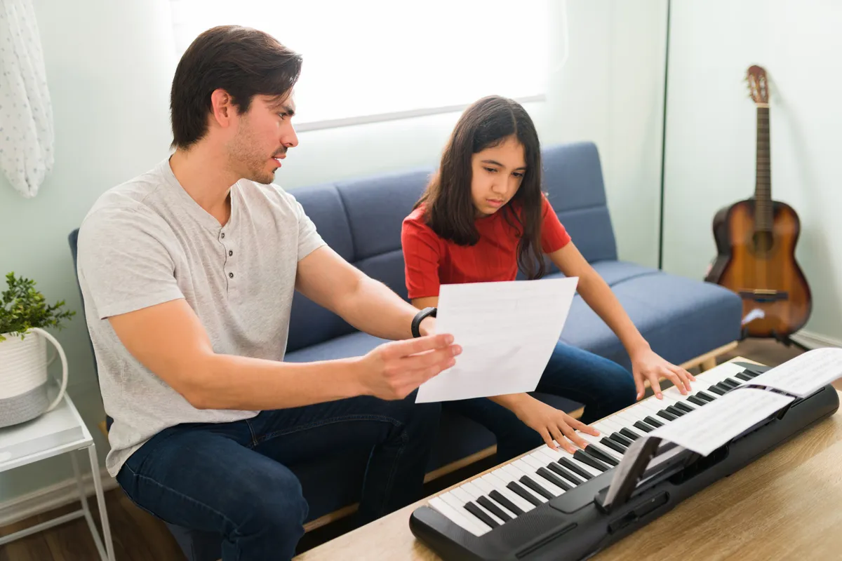 A music teacher helping a child read sheet music at a piano